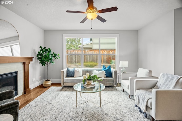 living room with wood-type flooring, a tile fireplace, a textured ceiling, and ceiling fan