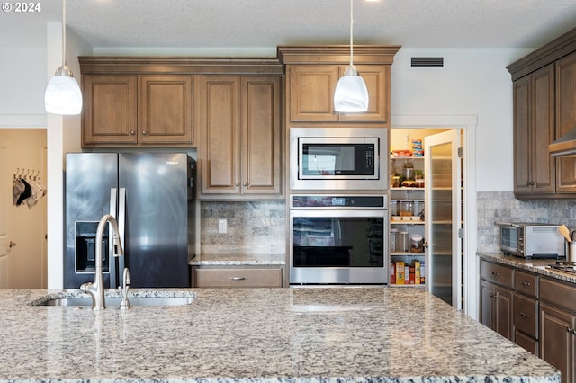 kitchen featuring decorative backsplash, light stone countertops, sink, decorative light fixtures, and stainless steel appliances