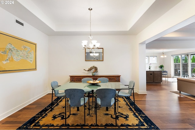 dining area with dark wood-type flooring, a tray ceiling, and a chandelier