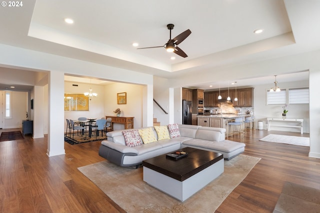 living room featuring a raised ceiling, ceiling fan with notable chandelier, and dark hardwood / wood-style flooring