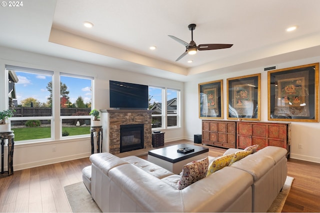 living room with ceiling fan, a stone fireplace, wood-type flooring, and plenty of natural light