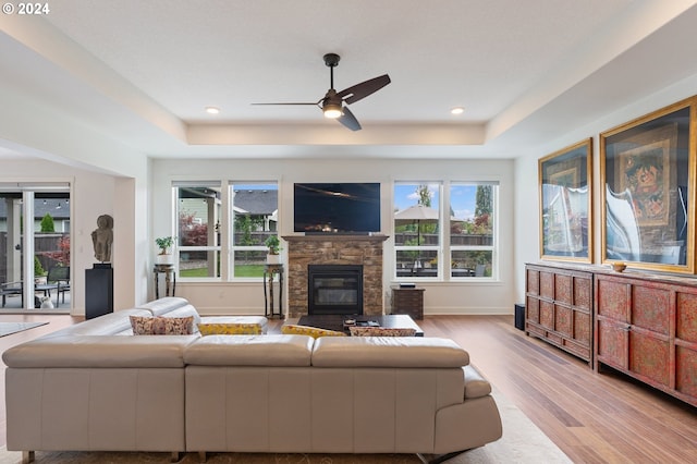 living room with a wealth of natural light, light hardwood / wood-style flooring, a stone fireplace, and ceiling fan