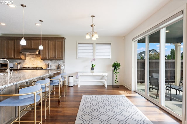 kitchen featuring dark wood-type flooring, light stone countertops, decorative backsplash, and hanging light fixtures