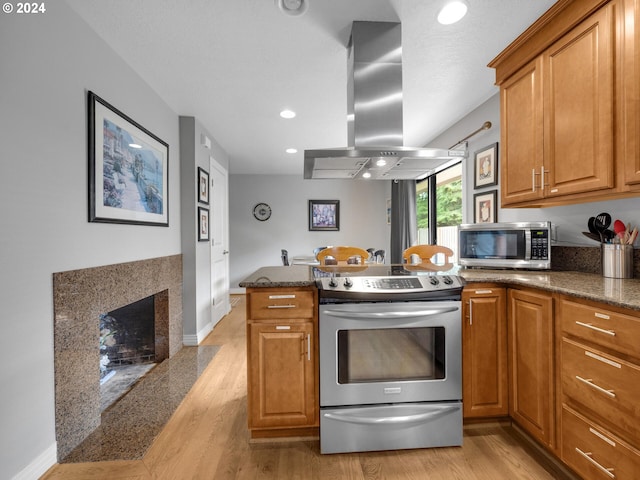 kitchen featuring dark stone countertops, island range hood, light hardwood / wood-style flooring, and stainless steel appliances