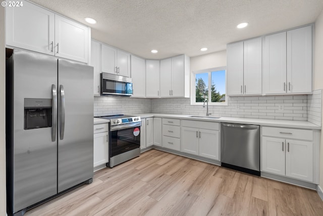 kitchen with sink, a textured ceiling, white cabinetry, light hardwood / wood-style floors, and stainless steel appliances