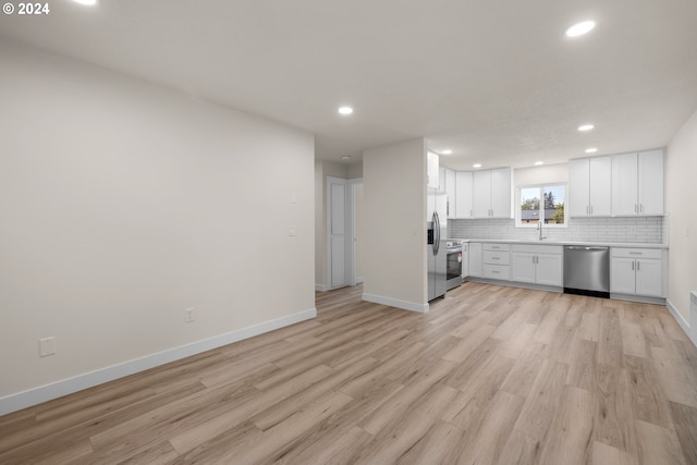 kitchen with appliances with stainless steel finishes, sink, white cabinets, decorative backsplash, and light hardwood / wood-style flooring