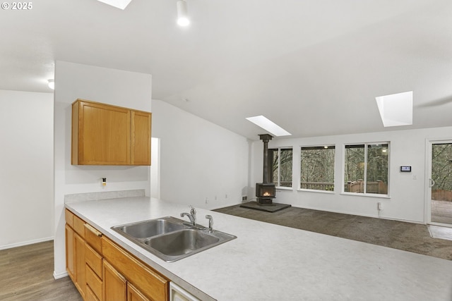 kitchen featuring hardwood / wood-style floors, a wood stove, sink, and lofted ceiling with skylight