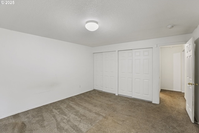 unfurnished bedroom with multiple closets, a textured ceiling, and dark colored carpet