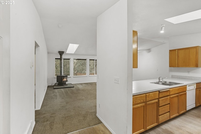 kitchen with a wood stove, lofted ceiling with skylight, sink, and white dishwasher