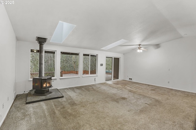 unfurnished living room featuring a wood stove, ceiling fan, carpet floors, and lofted ceiling with skylight