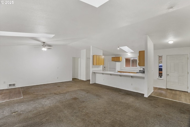 unfurnished living room with ceiling fan, vaulted ceiling with skylight, and dark carpet