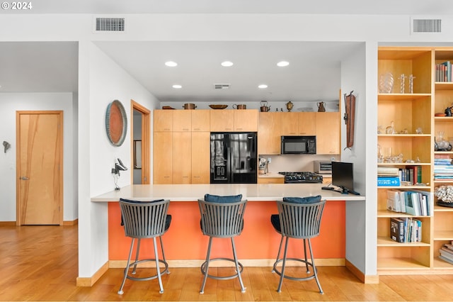 kitchen featuring light hardwood / wood-style floors, kitchen peninsula, black appliances, and a kitchen breakfast bar