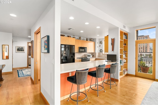 kitchen featuring built in desk, kitchen peninsula, black appliances, a kitchen bar, and light hardwood / wood-style floors