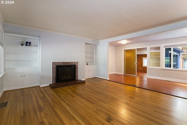 unfurnished living room featuring a fireplace, wood-type flooring, crown molding, and built in shelves