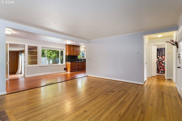 unfurnished living room featuring sink, light wood-type flooring, and ornamental molding