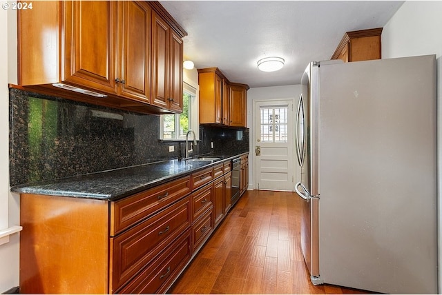 kitchen featuring hardwood / wood-style floors, dishwasher, sink, stainless steel fridge, and dark stone countertops