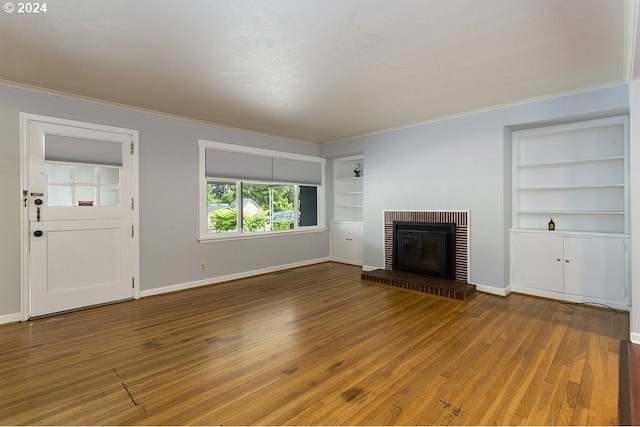 unfurnished living room with ornamental molding, built in features, wood-type flooring, and a brick fireplace