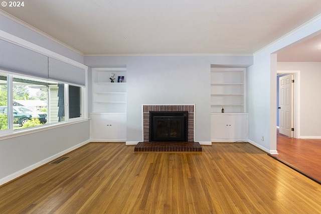 unfurnished living room with hardwood / wood-style flooring, built in shelves, crown molding, and a fireplace