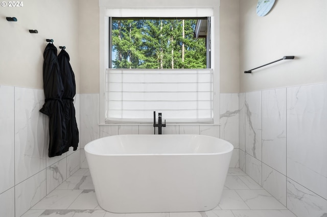 bathroom with a tub to relax in and tile walls