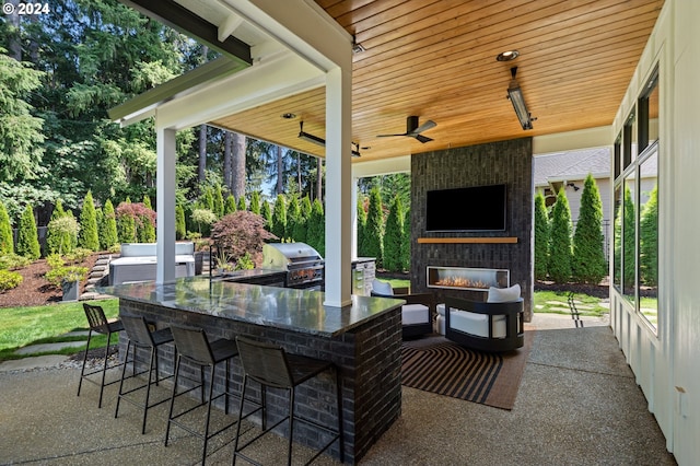 view of patio / terrace with ceiling fan, exterior kitchen, a grill, an outdoor bar, and a fireplace