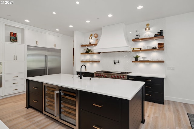 kitchen with custom range hood, sink, a center island with sink, wine cooler, and built in fridge