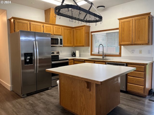 kitchen with sink, a center island, dark wood-type flooring, and appliances with stainless steel finishes