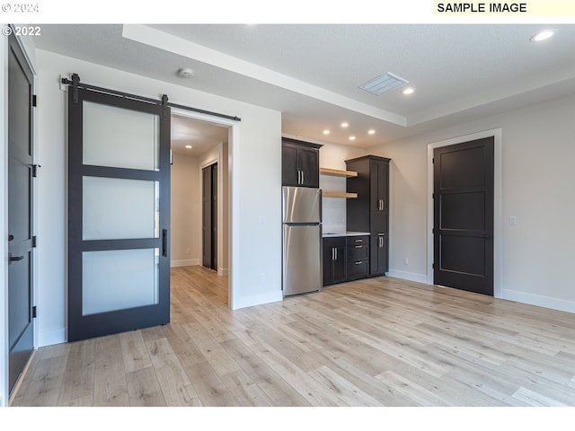 kitchen with a textured ceiling, light hardwood / wood-style flooring, a barn door, and stainless steel fridge