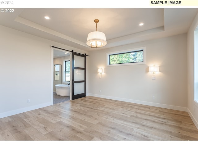 empty room with light hardwood / wood-style flooring, a barn door, and a tray ceiling