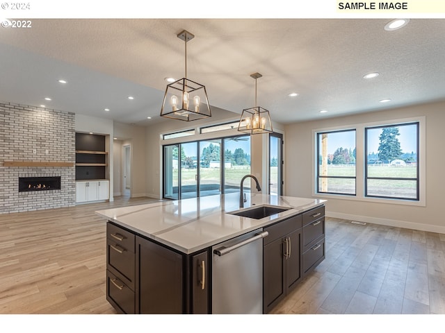 kitchen featuring dishwasher, an island with sink, light hardwood / wood-style flooring, hanging light fixtures, and sink