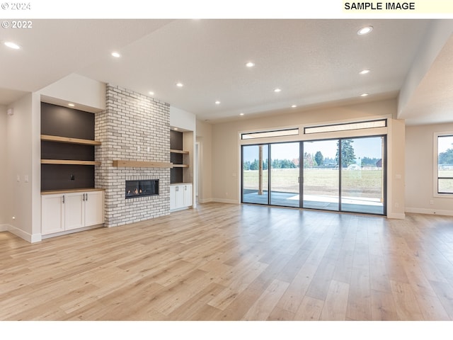 unfurnished living room with built in features, a brick fireplace, a textured ceiling, and light hardwood / wood-style floors