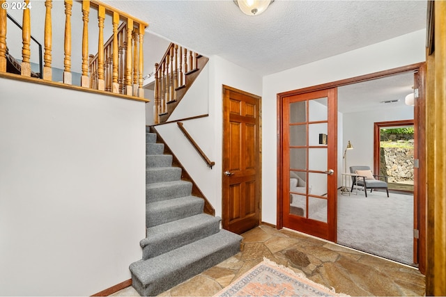 entryway featuring french doors, stone tile flooring, stairway, a textured ceiling, and baseboards