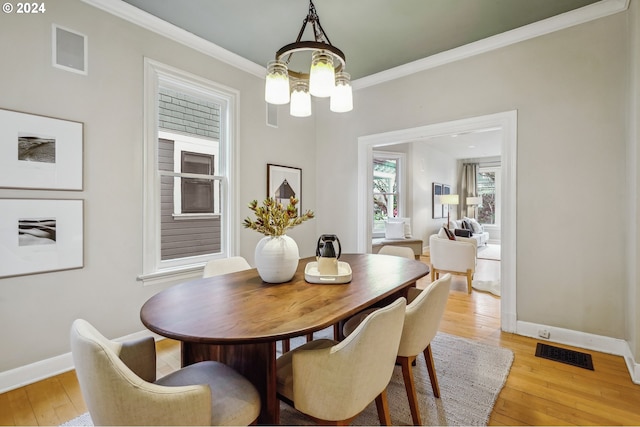 dining room with a chandelier, ornamental molding, and light wood-type flooring