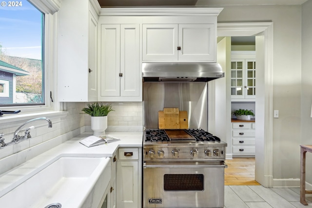 kitchen featuring designer range, white cabinetry, sink, and range hood