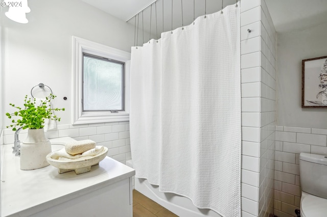 bathroom with toilet, shower / tub combo with curtain, and tile walls