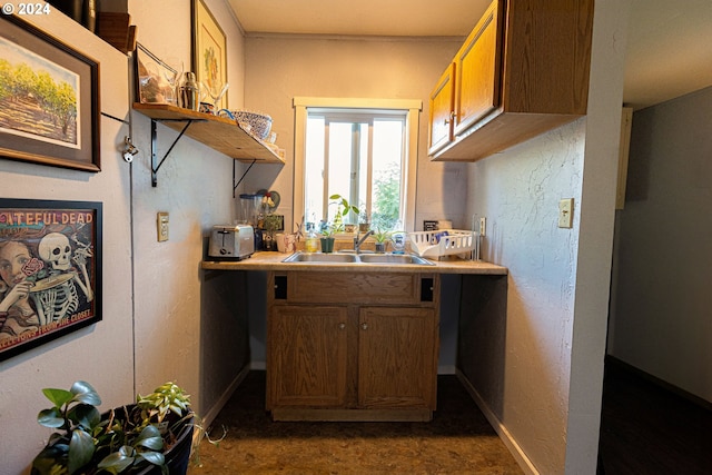 kitchen with baseboards, brown cabinetry, light countertops, open shelves, and a sink