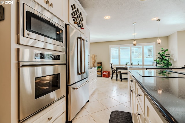 kitchen with stainless steel appliances, light tile patterned floors, hanging light fixtures, and white cabinets