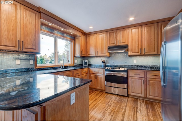 kitchen with dark stone counters, light wood-type flooring, sink, kitchen peninsula, and stainless steel appliances