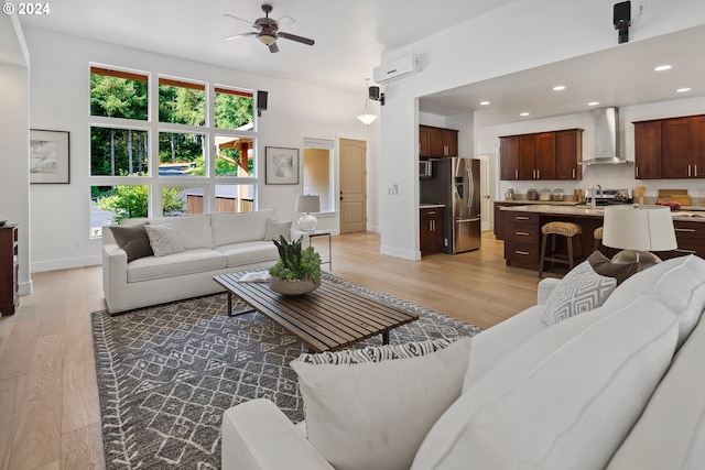 living room with a wall mounted air conditioner, ceiling fan, and light hardwood / wood-style flooring