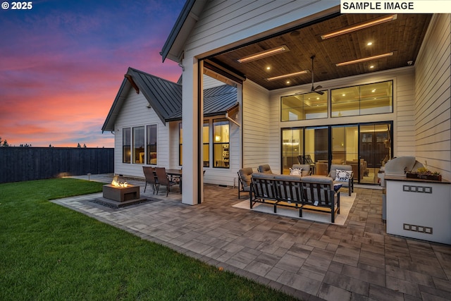 back house at dusk featuring ceiling fan, a patio area, a yard, and an outdoor living space with a fire pit