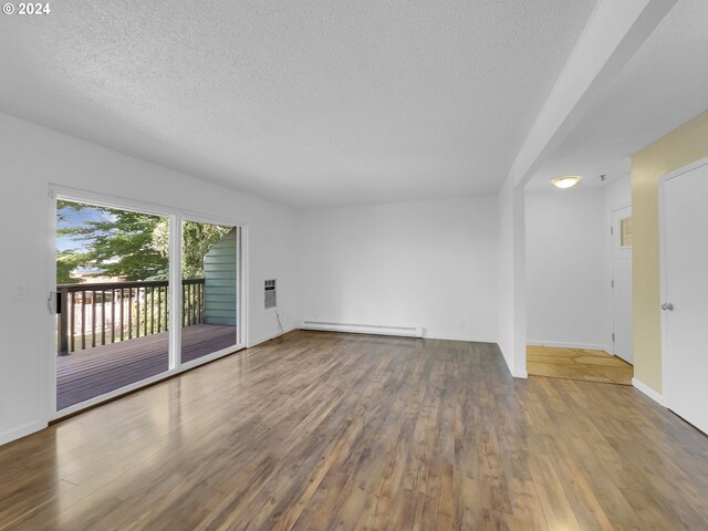 unfurnished living room with a textured ceiling, baseboard heating, and wood-type flooring