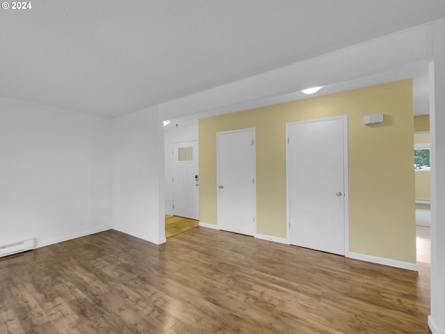 empty room with wood-type flooring and a baseboard heating unit