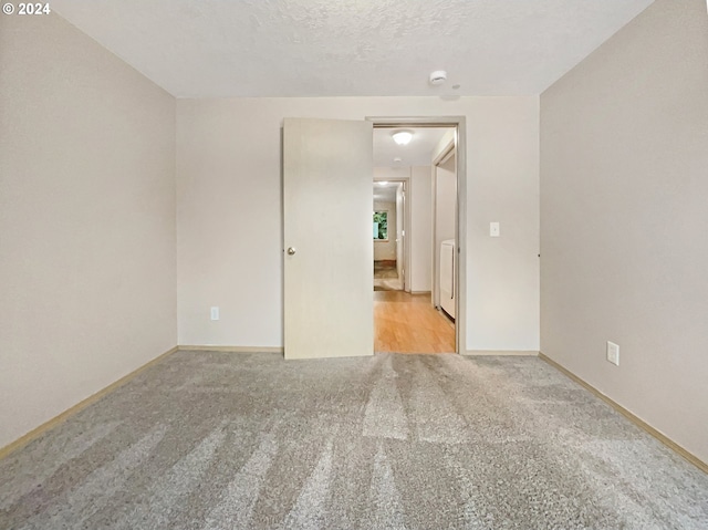 unfurnished room with light carpet, a textured ceiling, and washer / clothes dryer