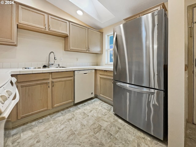 kitchen featuring white appliances, sink, vaulted ceiling with skylight, tile counters, and light brown cabinets