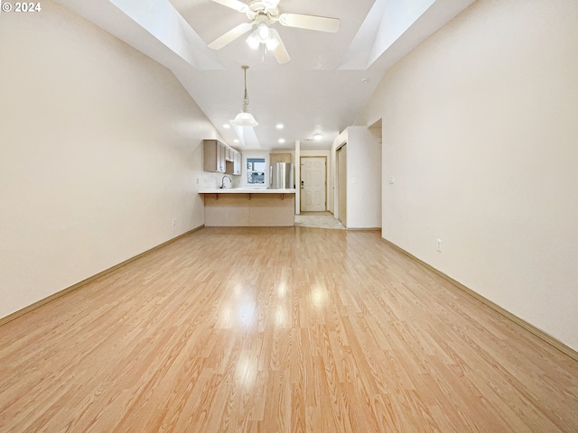 unfurnished living room with ceiling fan, vaulted ceiling with skylight, and light hardwood / wood-style flooring