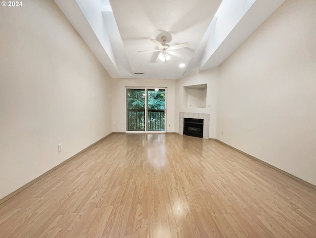 unfurnished living room with a tiled fireplace, ceiling fan, lofted ceiling, and light wood-type flooring