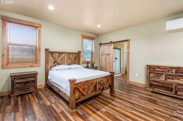 bedroom with dark hardwood / wood-style flooring, a barn door, and a wall mounted air conditioner