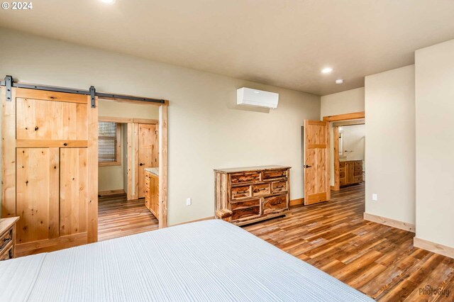 bedroom with a wall unit AC, hardwood / wood-style floors, ensuite bathroom, and a barn door