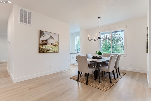 dining area with sink, light hardwood / wood-style flooring, and a notable chandelier