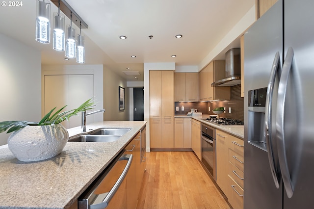 kitchen with stainless steel appliances, decorative light fixtures, wall chimney range hood, light stone counters, and sink