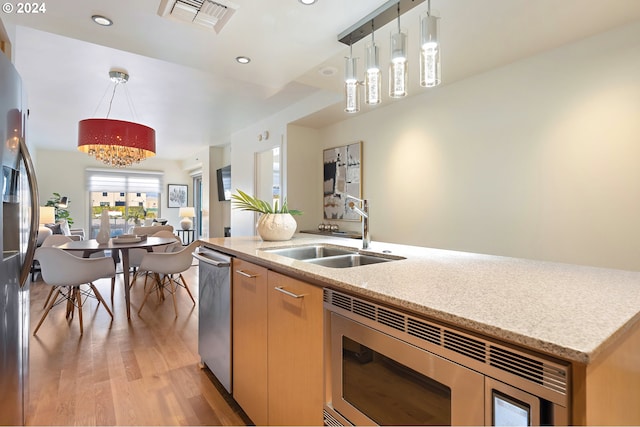 kitchen featuring sink, light hardwood / wood-style flooring, hanging light fixtures, light stone countertops, and stainless steel appliances